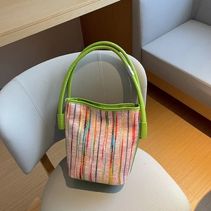 Sac seau chic à rayures multicolores avec poignée vert vif posé sur un fauteuil