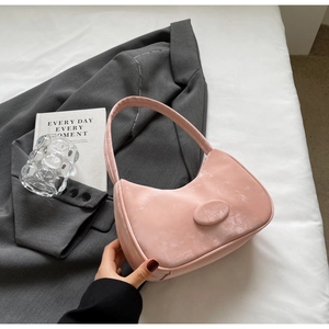 Dettaglio della borsa hobo in velluto rosa con logo rotondo su sfondo giacca grigia