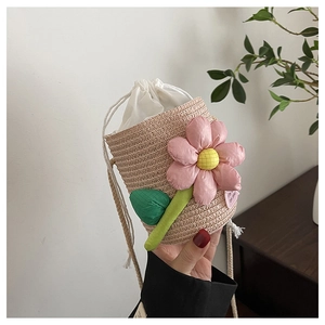 Detail of hand-woven straw bucket bag featuring a large pink fabric flower and drawstring lining