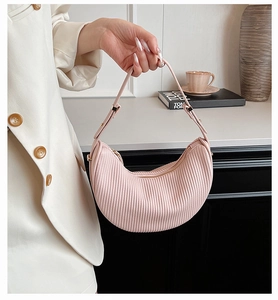 Detail of light pink pleated dumpling bag held by model in an elegant studio setting