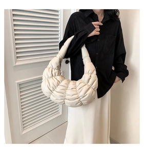 Close-up of beige pleated cloud bag featuring soft quilted texture and minimalist crescent shape