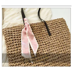 Detail of woven straw beach bag featuring a pink heart print scarf wrapped on the handle