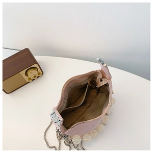 Detailopname van roze crossbodytas met golfvoering en parelketting schouderband