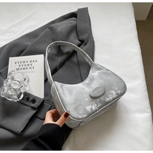 Borsa sottospalla in velluto argento metallizzato con logo accanto a un blazer grigio