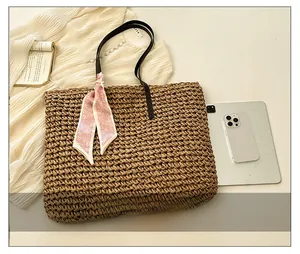 Detail of woven straw tote bag featuring leather handles and pink heart scarf decor