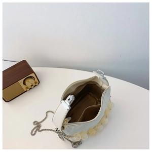 Detail van de beige kunstlederen tas met kralenhandvat en zilveren metalen ketting
