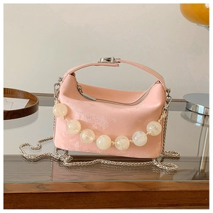 Detail van roze suède crossbodytas met parelriem en zilveren ketting op een tafelblad