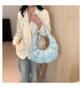 Fashionable light blue pleated cloud bag shown on shoulder in a stylish indoor setting