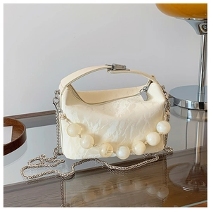 Detail van crème crossbodytas van plooileer met decoratie van grote marmeren kralen