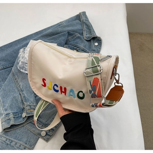 Close-up of cream canvas crossbody bag featuring letter embroidery and wide floral strap