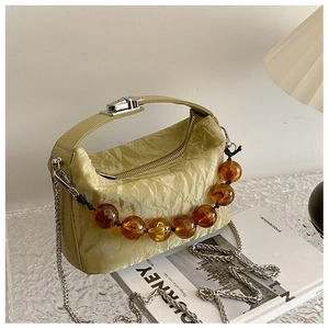 Detail van geplooide leren tas met amberkleurige kralenketting en zilveren draaislot