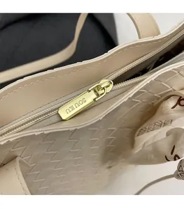 Detailed close-up of golden zipper pull with branding on beige woven tote bag