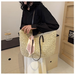 Detail of a beige woven straw tote bag with brown leather straps and a pink heart scarf