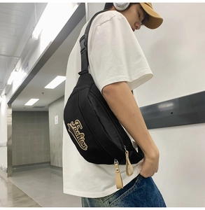 Détail du sac bandoulière noir avec broderie 'Fashion' et tirette de zip en cuir
