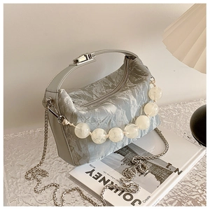 Detail van lichtblauwe geplooide handtas met zilveren ketting en witte decoratieve kralen