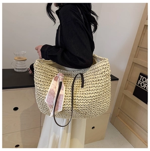 Close-up of a woven straw tote bag with a pink silk scarf and brown shoulder straps