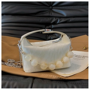 Detail van witte handtas met plissétextuur, grote sierparels en zilverkleurige ketting