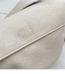 Close-up of the embossed logo and pleated leather texture on a beige crossbody bag