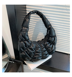 Detail of black pleated croissant bag with glossy leather texture and puffy crescent shape