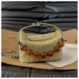 Detail van lichtgroene geplooide handtas met amberkleurige kralen en zilveren ketting