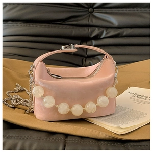 Detail van roze suède handtas met een decoratieve ketting van grote witte kralen afwerking
