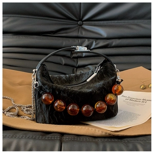 Detail van zwarte geplooide crossbodytas met amberkleurige kraal en zilveren ketting