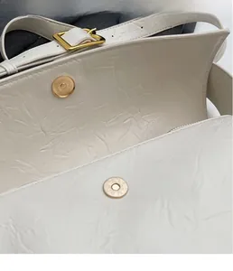 Detail view of cream shoulder bag with pleated leather texture and gold magnetic snaps