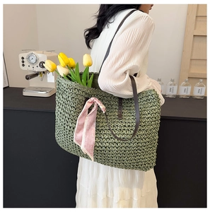 Detail of green woven straw shoulder bag with pink heart scarf and leather straps