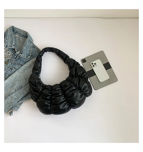 Flat lay of black pleated cloud bag shown with denim jacket and electronic devices