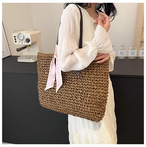 Detail of a large brown straw tote bag with a pink heart silk scarf worn by a model