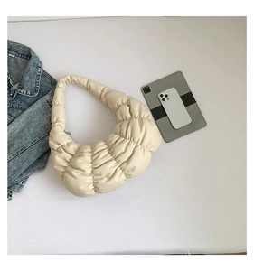 Detail view of cream pleated cloud bag showing soft texture next to a tablet and phone