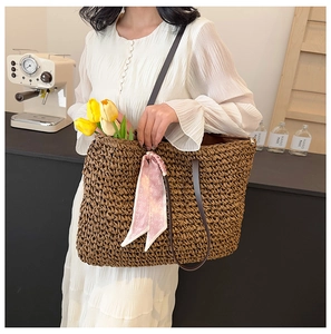 Close-up of large woven straw tote with leather strap and pink heart silk scarf detail