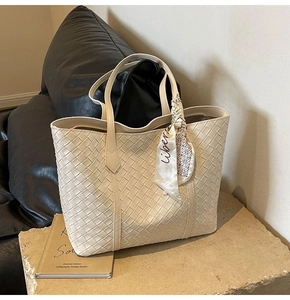 Detail of beige woven tote bag with silk scarf on a stone pedestal in a studio setting