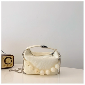 Detail van crèmekleurige handtas met geplooide textuur, kralen en zilveren ketting