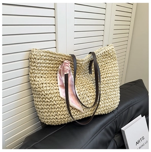 Close-up of cream woven straw tote with slim brown leather straps and pink scarf detail