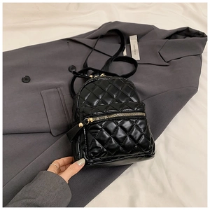 Close-up of black quilted mini backpack with gold zippers on a dark blazer background