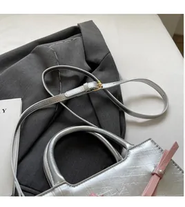 Close-up of silver tote bag with pink bow, pearl accent, and long shoulder strap