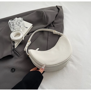 Macro detail of white pleated crescent bag with gold hardware on a grey suit jacket