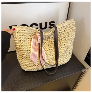 Detail of hand-woven straw tote with brown leather straps and pink heart-patterned silk scarf