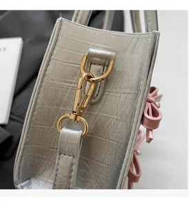 Detail of silver crocodile embossed handbag with pink bow and gold metal hardware