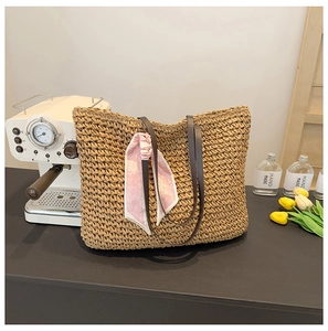 Detail of large straw tote bag with brown leather straps and pink heart scarf decoration