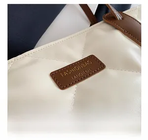 Close-up of quilted white tote bag featuring a leather logo patch and brown handles