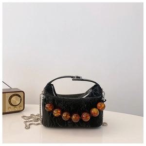 Detail van zwarte crossbodytas met grote amberkleurige kralen en metalen kettingriem