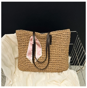 Close-up of woven straw tote bag with brown leather straps and pink heart silk scarf detail