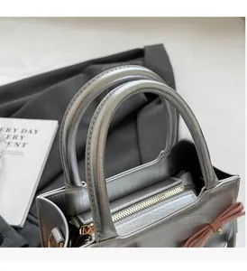 Close-up of silver tote bag with dual circular handles and pink bow detail