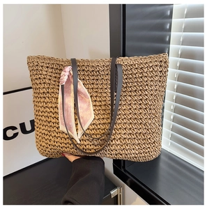 Detail of woven straw tote bag with black leather straps and pink heart print scarf