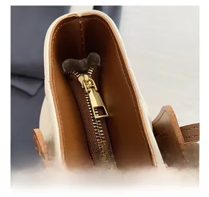Close-up of smooth gold metal zipper and leather stitching on beige shoulder bag