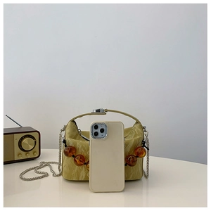 Detail van compacte mosterdkleurige crossbodytas met harskralen en ketting naast een telefoon