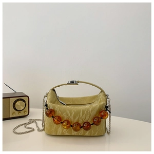 Detail van crème geplooide crossbodytas met amberkleurige kralenketting en metalen riem