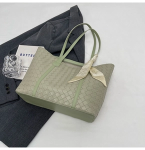 Close-up of sage green woven tote bag with a silk scarf detail on a workspace background